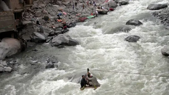 Menschen überqueren einen Fluss mithilfe einer Seilbahn. (Foto: Naveed Ali/AP/dpa)