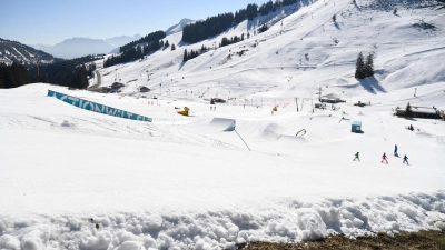 Während sich im Vordergrund schon das erste Grün zeigt, fahren Skifahrer eine Piste hinunter. (Foto: Uwe Lein/dpa/Archiv)