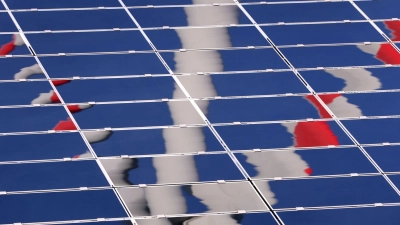 Ein Windrad spiegelt sich in eine Photovoltaik-Anlage eines Solarparks. (Foto: Karl-Josef Hildenbrand/dpa)