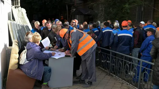 Bauarbeiter stellen sich bei einem mobilen Wahllokal in der von Russland unterstützten und von Separatisten kontrollierten Volksrepublik Donezk an, um ihre Stimmzettel für das Scheinreferendum zu holen. (Foto: Uncredited/AP/dpa)