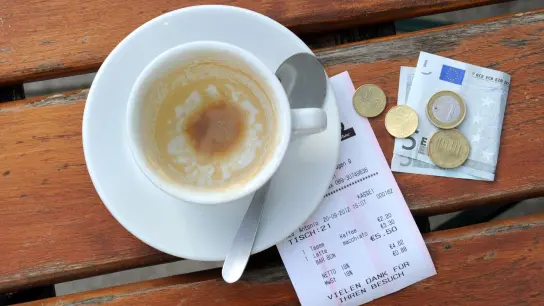 Münzen, ein Geldschein und eine Rechnung liegen neben einer leeren Kaffeetasse auf einem Tisch in einem Restaurant. (Foto: Tobias Hase/dpa)
