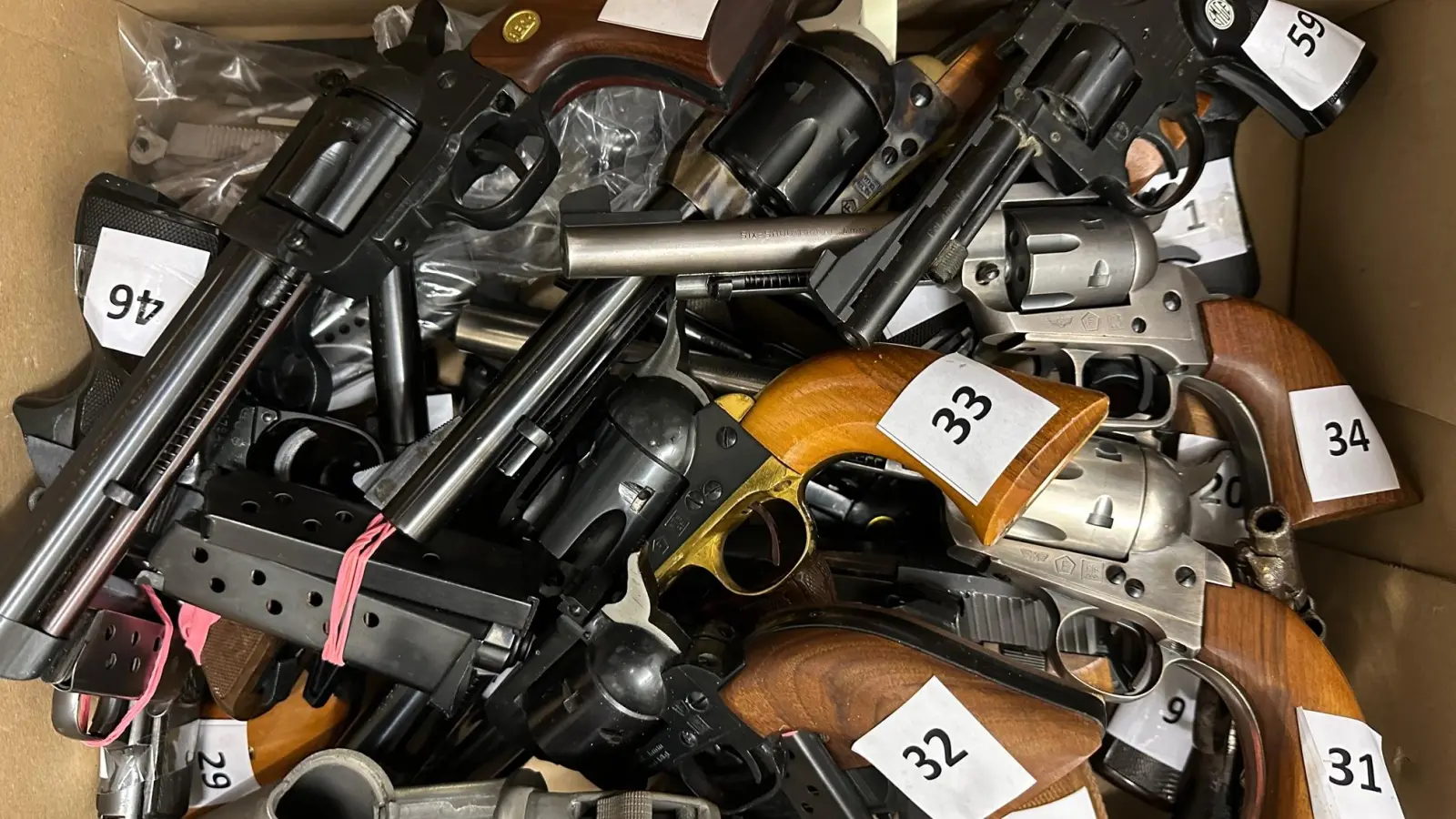 Das Bild zeigt verschiedene, von den zuständigen Beamten des Landratsamt Ansbach asservierte Feuerwaffen aus privatem Besitz, hauptsächlich Kurzwaffen, unter anderem eine halbautomatische Kurzwaffe, nämlich die Pistole mit der nach unten zeigenden Nummer 46. (Foto: Landratsamt Ansbach/Fabian Hähnlein)