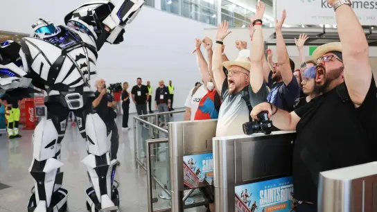 Computerspiel-Fans feiern gemeinsam mit einem Roboter den Einlass zur Messe. (Foto: Oliver Berg/dpa)