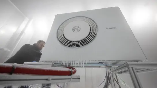 Ein Mitarbeiter der Bosch Thermotechnik GmbH öffnet in einer Klimakammer das Gehäuse einer Bosch-Wärmepumpe. (Foto: Marijan Murat/dpa)
