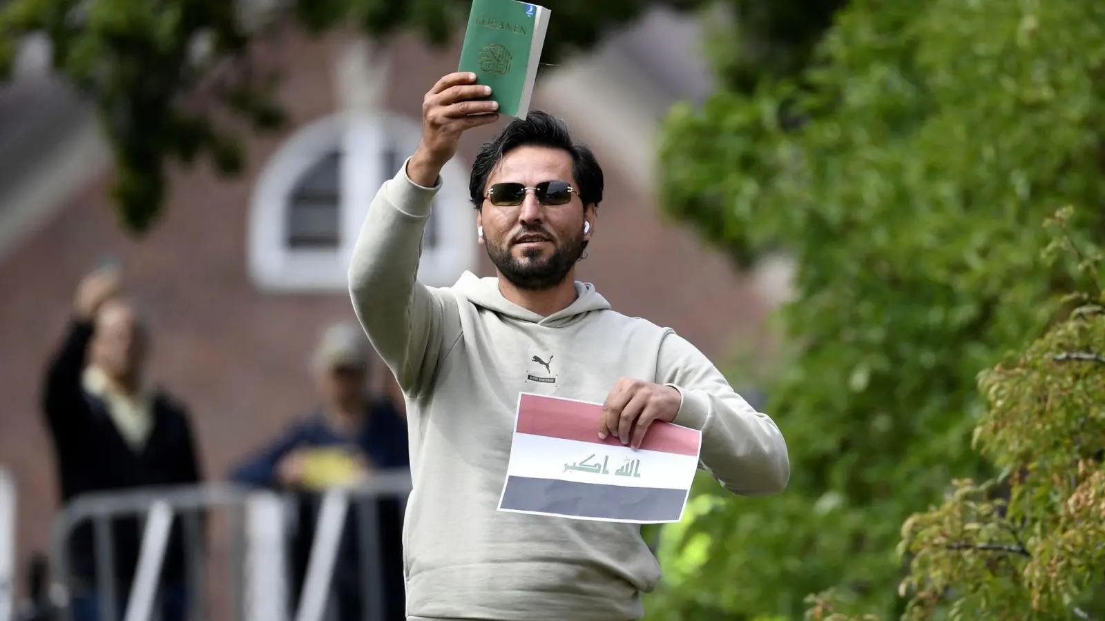 Ein Demonstrant hält eine Kopie des Korans hoch, die er mutmaßlich gemeinsam mit einer irakischen Fahne verbrennen will. (Foto: Oscar Olsson/TT NEWS AGENCY/AP/dpa)