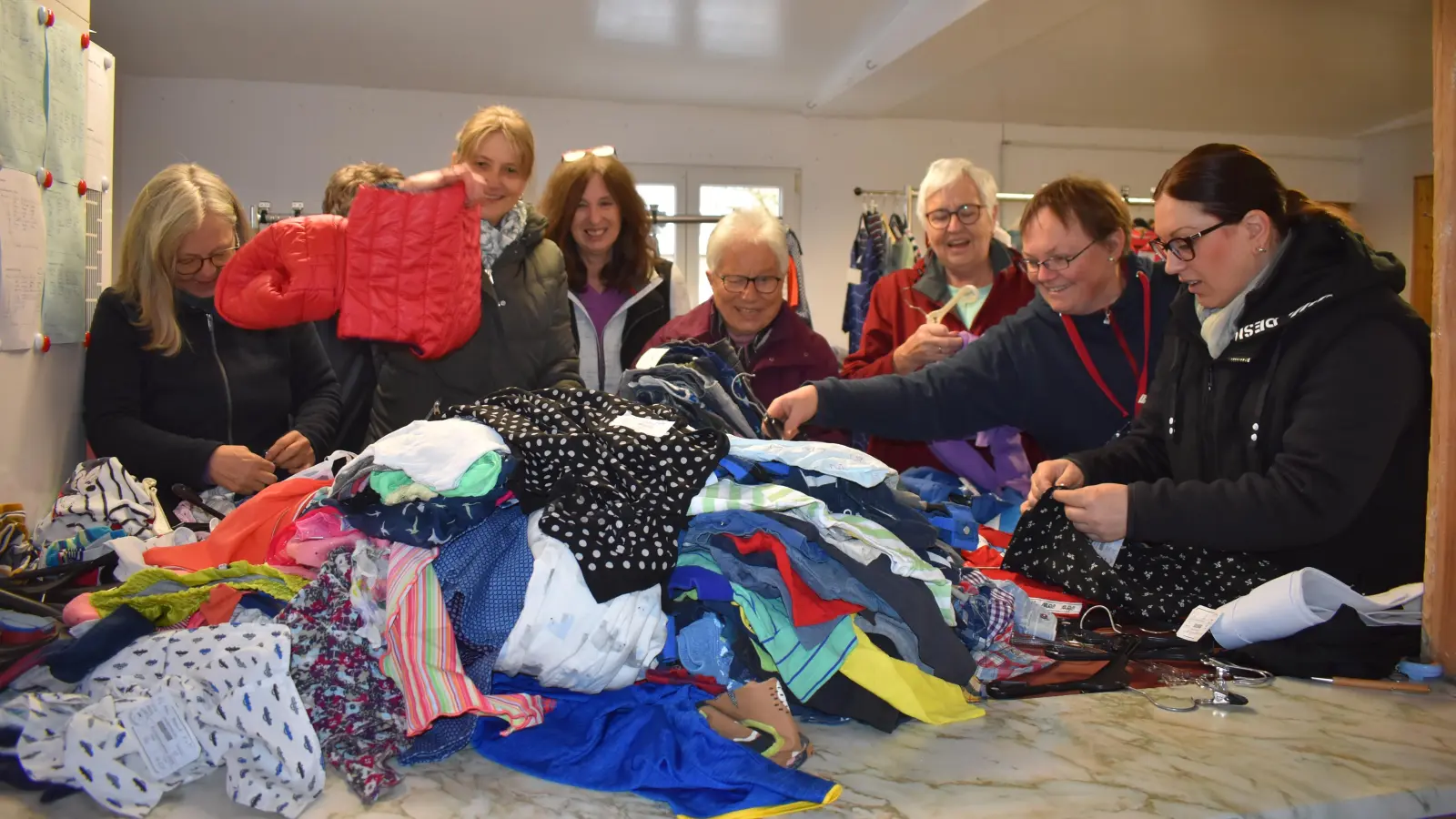 Alle Hände voll zu tun haben die gut gelaunten ehrenamtlichen Helferinnen der KATZE, die die angelieferten Bekleidungsberge auf Bügel hängen, bevor sie in den Verkauf gehen. (Foto: Ute Niephaus)