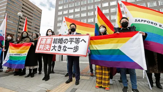 Anwälte der Kläger und Unterstützer halten 2021 Regenbogenflaggen und ein Transparent mit der Aufschrift: „Verfassungswidriges Urteil“ vor dem Bezirksgericht Sapporo hoch. (Foto: Yohei Fukai/Kyodo News/AP/dpa)