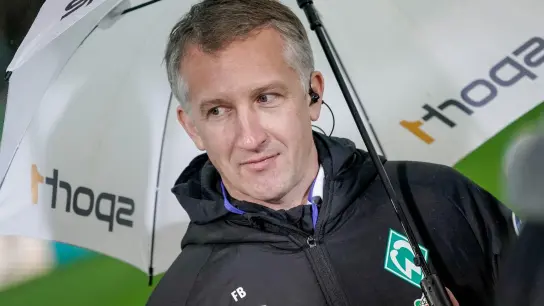 Bremens Geschäftsführer Frank Baumann steht mit einem Regenschirm am Spielfeldrand. (Foto: Axel Heimken/dpa)