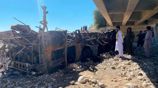 Menschen betrachten das verbrannte Wrack eines verunglückten Busses, der mit rund 50 Menschen an Bord in eine Schlucht gestürzt ist. (Foto: Muhammad Saleem/AP/dpa)
