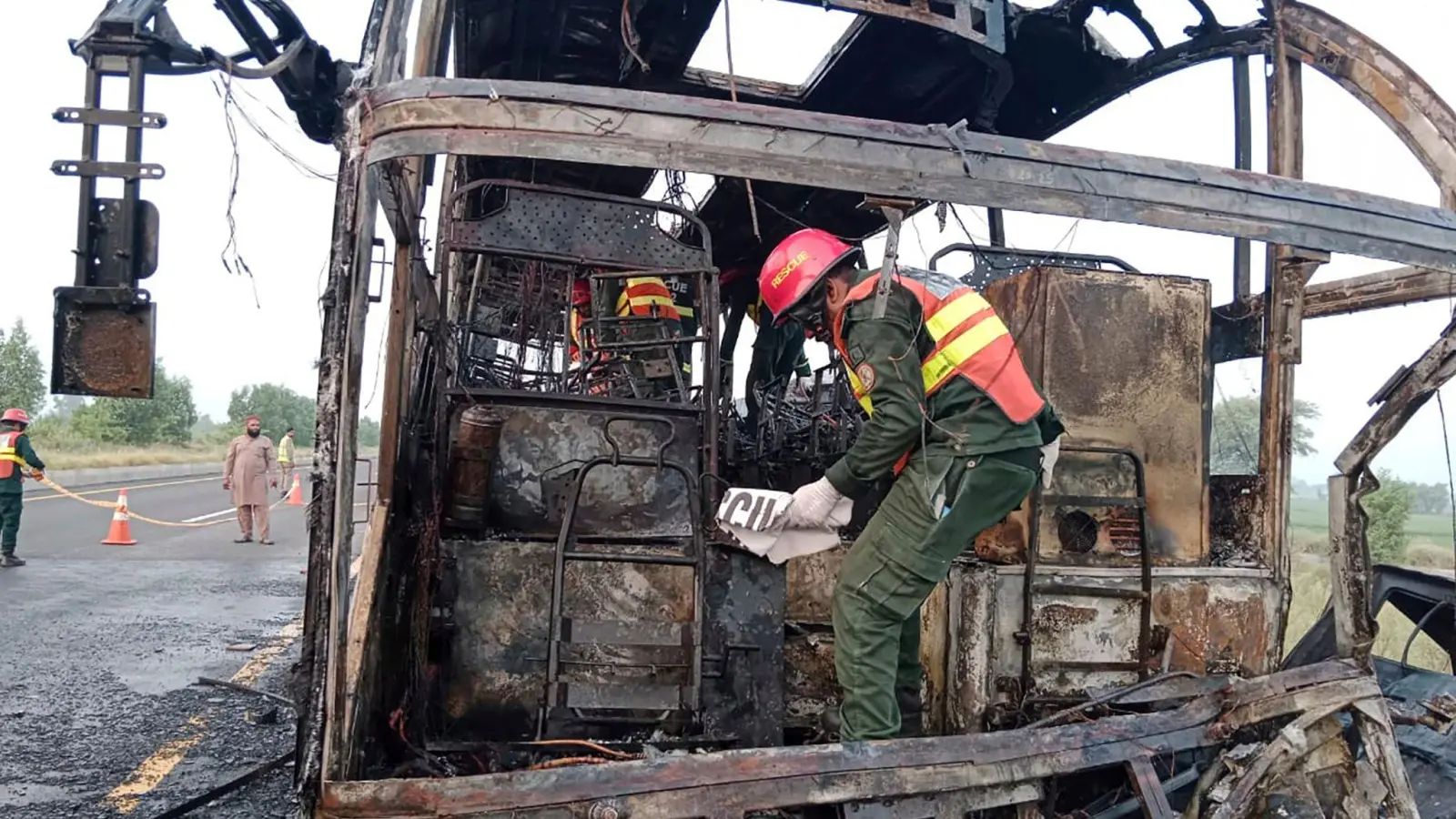 Rettungskräfte untersuchen den verbrannten Bus an der Unfallstelle auf einer Autobahn. (Foto: Uncredited/Rescue 1122 Emergency Department/AP/dpa)