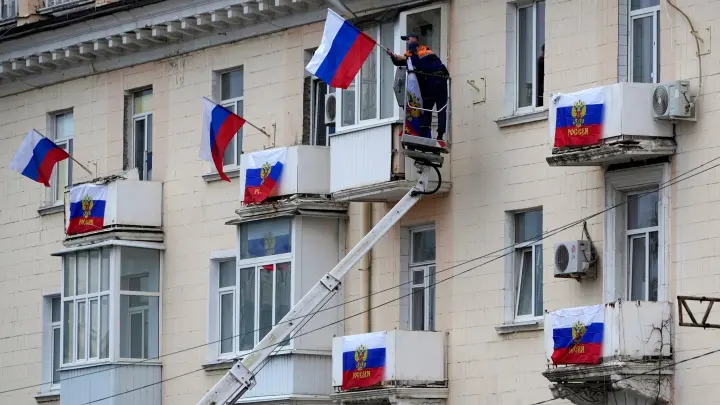 Arbeiter hängen russische Fahnen an einem Wohnhaus in der von Russland unterstützten und von Separatisten kontrollierten Volksrepublik Luhansk auf. (Foto: Uncredited/AP/dpa)