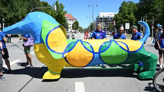 Ein bunter Riesendackel in den olympischen Farben fährt bei einer Parade mit. (Foto: Felix Hörhager/dpa)