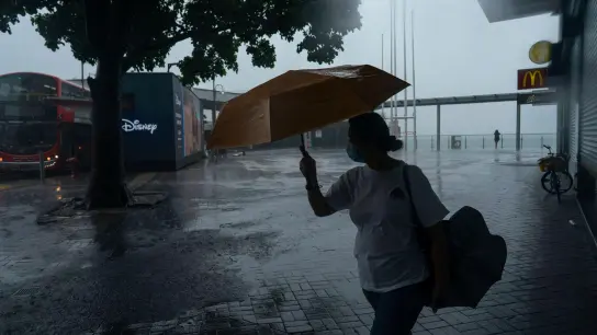 Eine Frau hält einen Regenschirm bei starkem Wind in der Nähe der Promenade von Victoria Habour, als der Tropensturm „Ma-on“ an Hongkong vorbeizieht. (Foto: Anthony Kwan/AP/dpa)