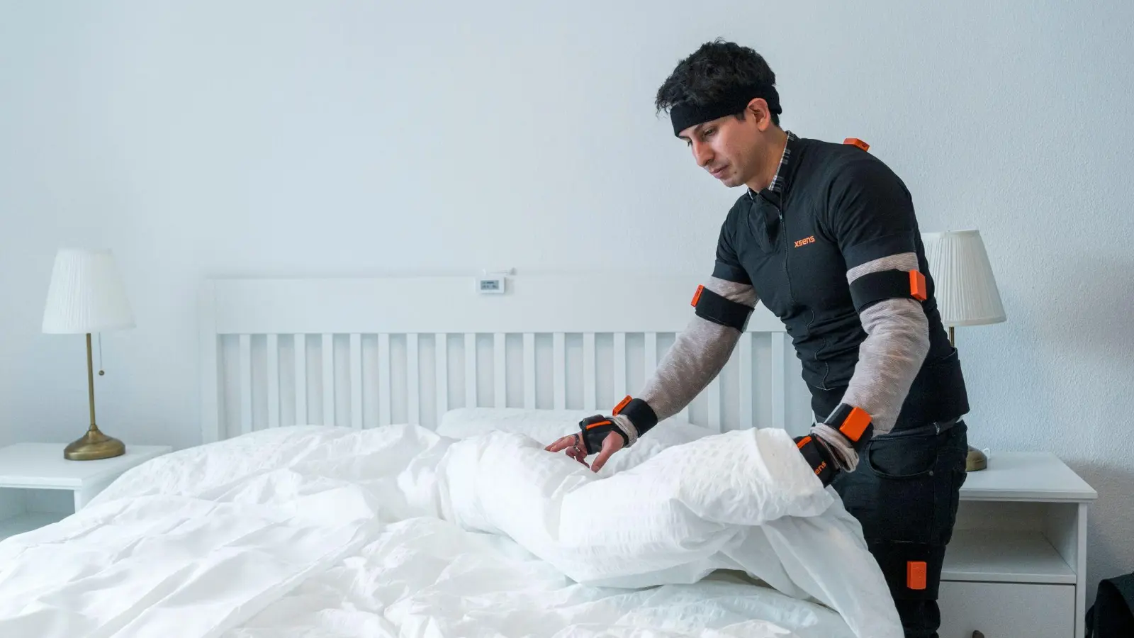 Doktorand Renato Mio räumt ein Bett auf, während er Bewegungssensoren trägt. (Foto: Daniel Vogl/dpa)