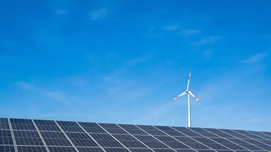 Ein Windrad hinter einem Solarfeld. Ab dem 1. Juli müssen Stromkunden die Förderung des Ökostroms nicht mehr über die Stromrechnung zahlen. (Foto: Peter Kneffel/dpa)