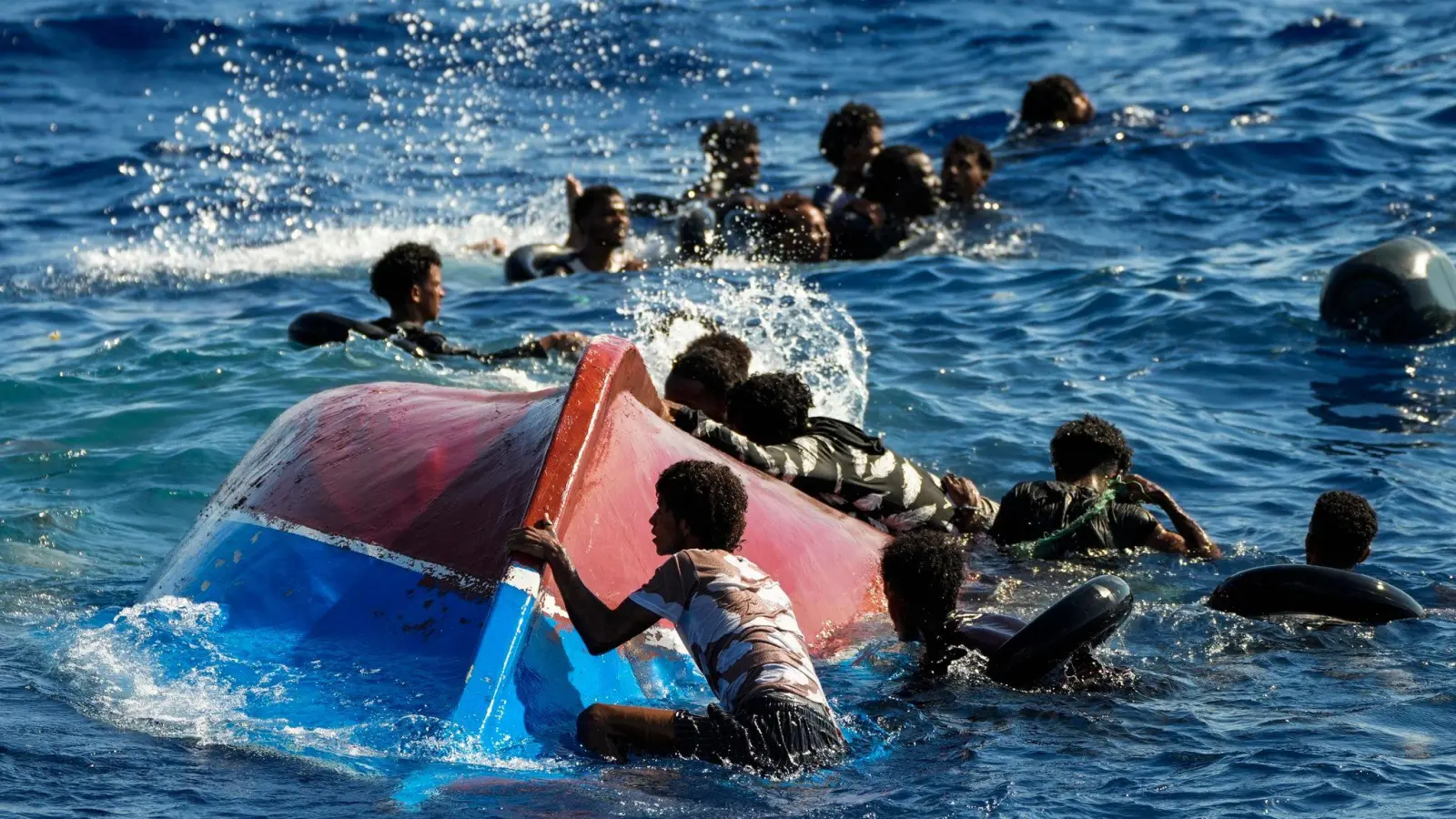 Migranten schwimmen neben ihrem umgestürzten Holzboot im Mittelmeer (Archiv). (Foto: Francisco Seco/AP/dpa)