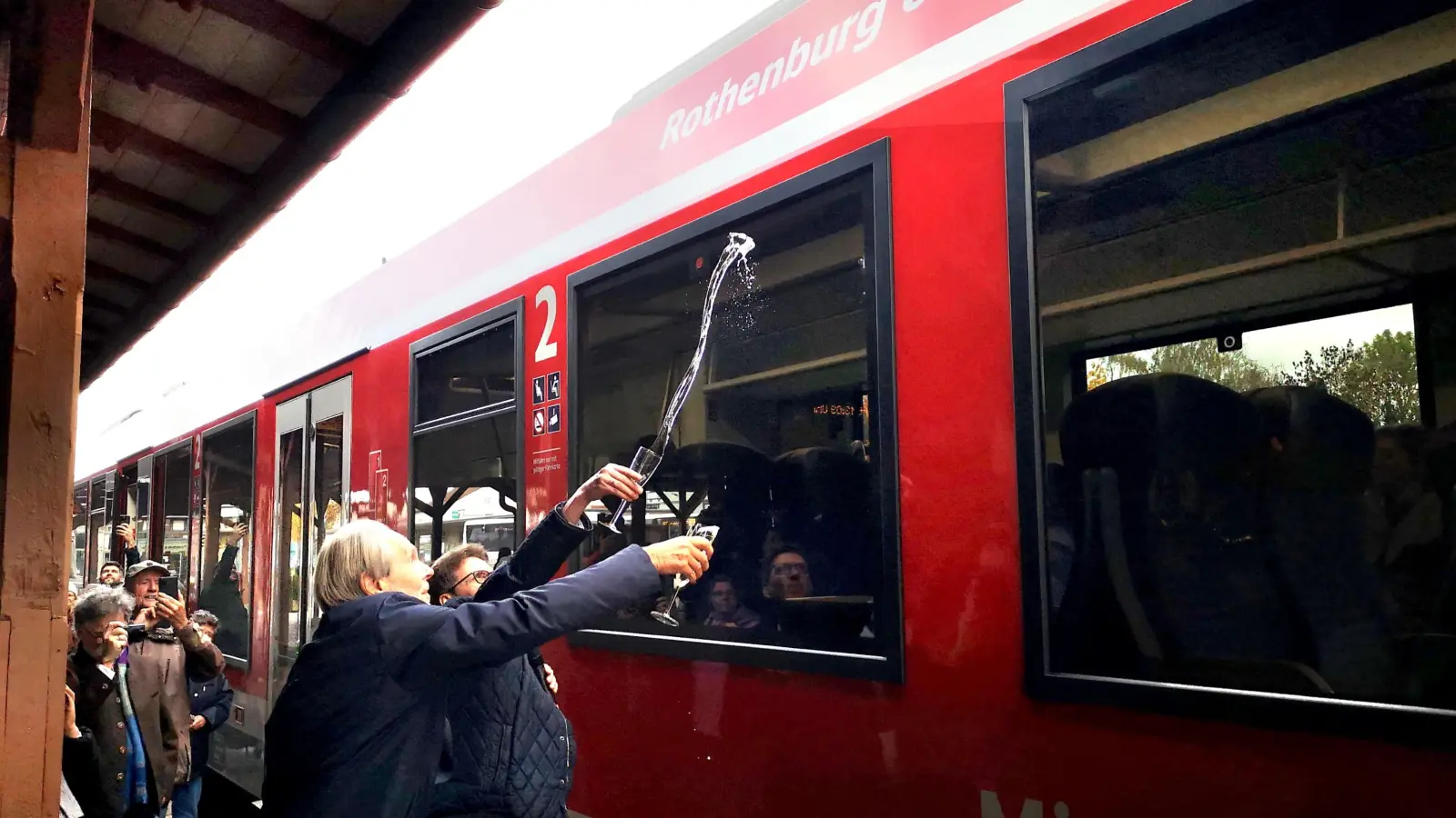 Der Zug bekam auch ein Schlückchen Sekt ab. Zweiter Bürgermeister Dieter Kölle und Bahn-Vertreter Marco Schimmich kippten den Inhalt ihrer Gläser – nicht ganz synchron – gegen die Wagenscheibe. (F.: Jürgen Binder)