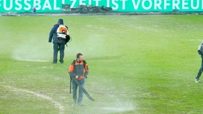 Arbeiter versuchten, Wasserlachen vom Spielfeld im Ludwigsparkstadion zu entfernen. (Foto: Uwe Anspach/dpa)