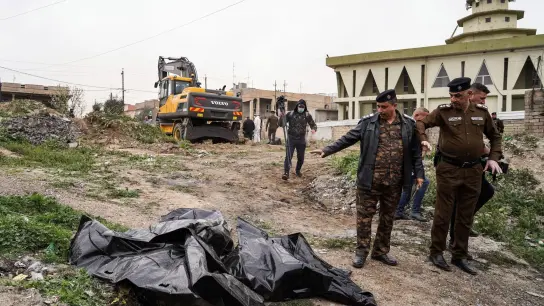 Mitglieder der Sicherheitskräfte zeigen auf einen Leichensack mit menschlichen Überresten, der in einem Massengrab im Westen von Mossul entdeckt wurde. Es wird angenommen, dass es sich dabei um die Opfer handelt, die während der Besetzung des Gebiets durch die Terrorgruppe Islamischer Staat (IS) im Jahr 2014 getötet und verscharrt wurden. (Foto: Ismael Adnan/dpa)