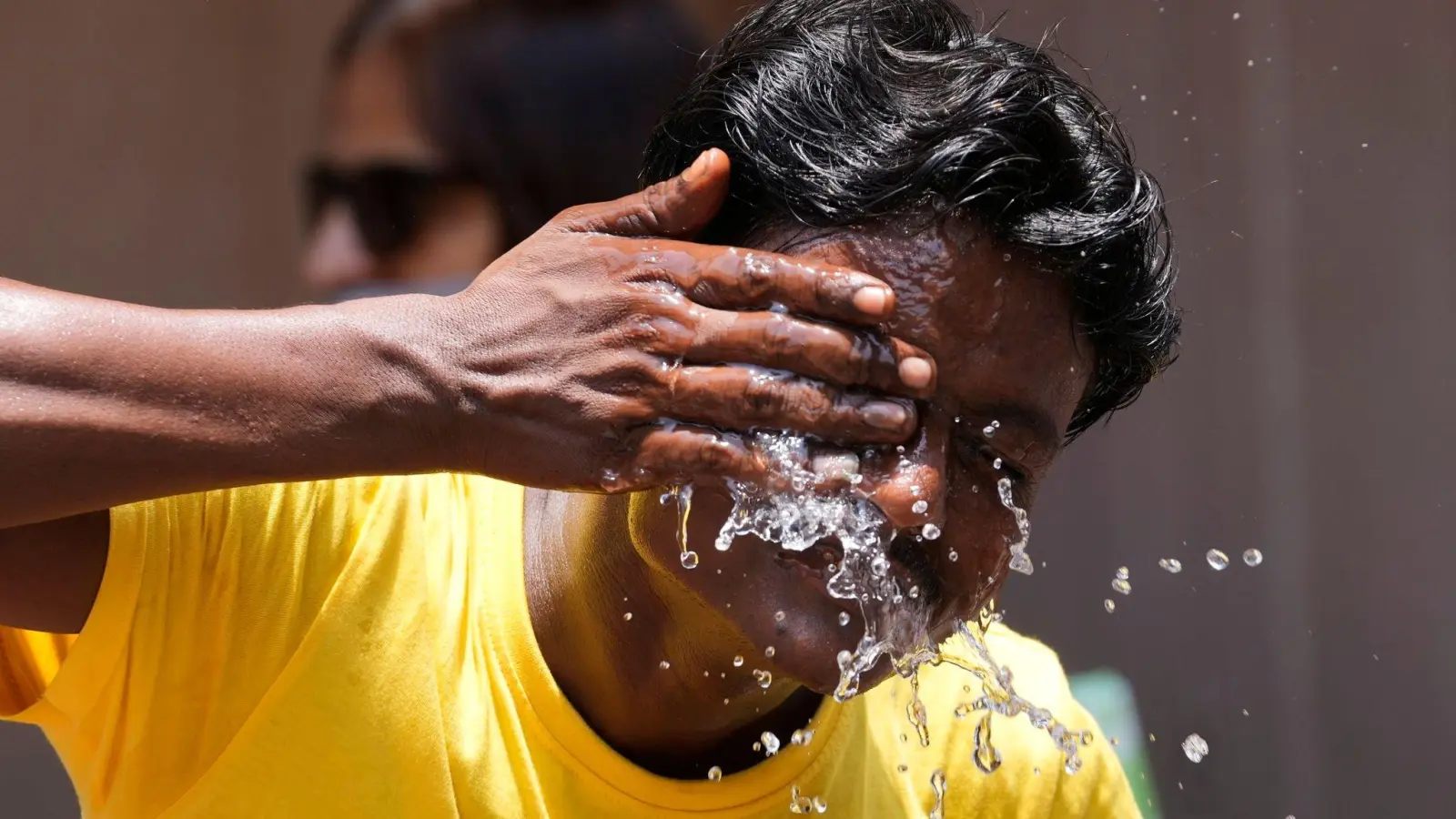 Ein Mann spritzt sich an einem extrem heißen Tag auf einem Marktplatz in Mumbai Wasser ins Gesicht. (Foto: Rajanish Kakade/AP/dpa)