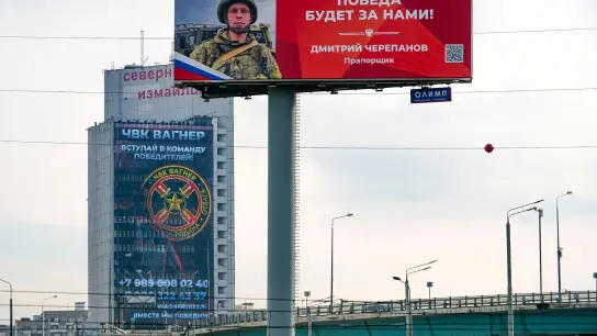 Ein Werbeschild, auf dem für das Militärunternehmen Wagner (hinten) geworben wird und auf dem zu lesen ist „Schließen Sie sich dem Team der Sieger an“. (Foto: Alexander Zemlianichenko/AP/dpa)