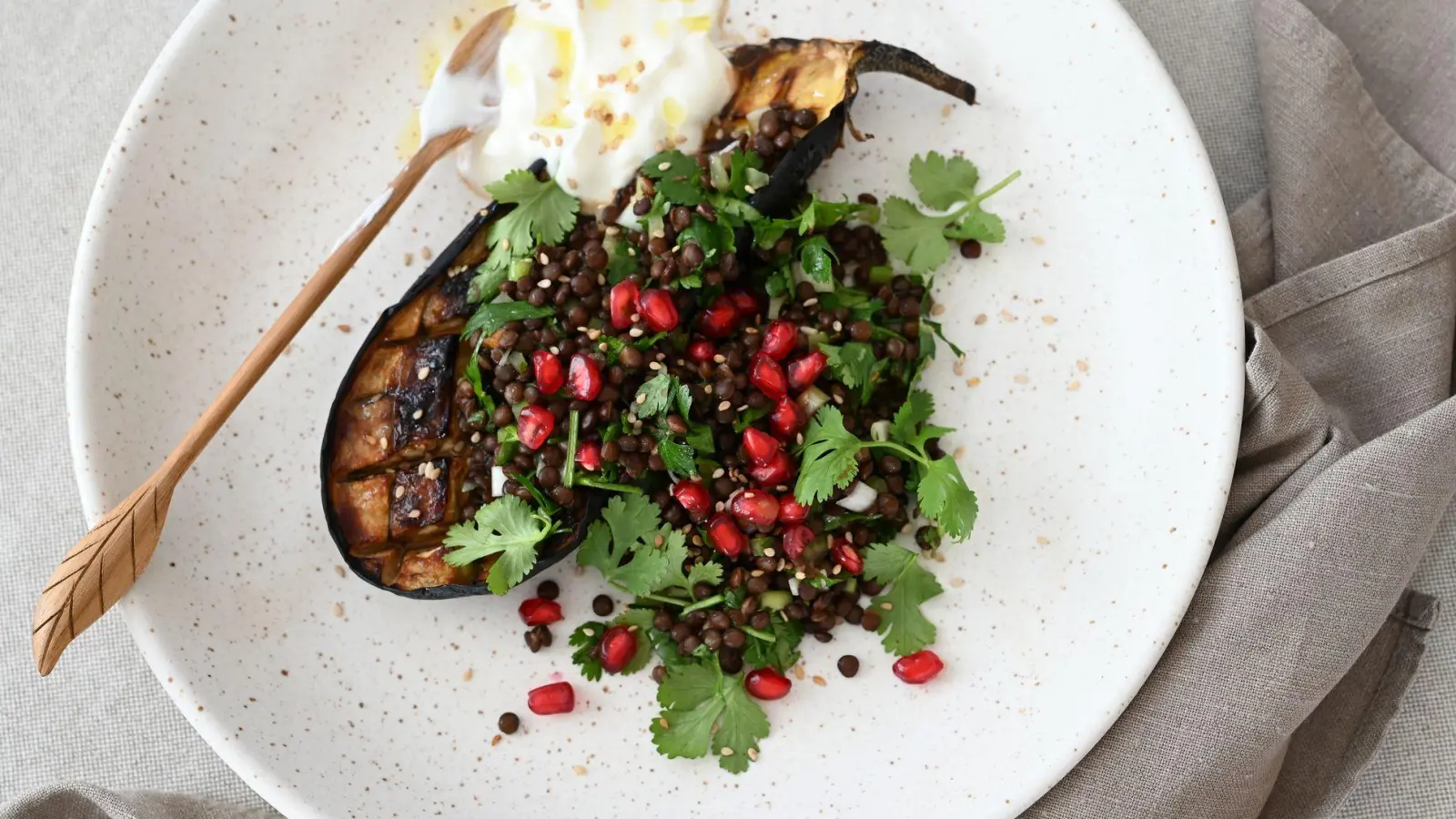 Ein Teller voller Kontraste und orientalischem Twist: Geschmorte Auberginen, getoppt mit Linsen-Kräuter-Salat, Granatapfelkernen und einem Klecks cremigem Joghurt. (Foto: Julia Uehren/dpa-tmn)
