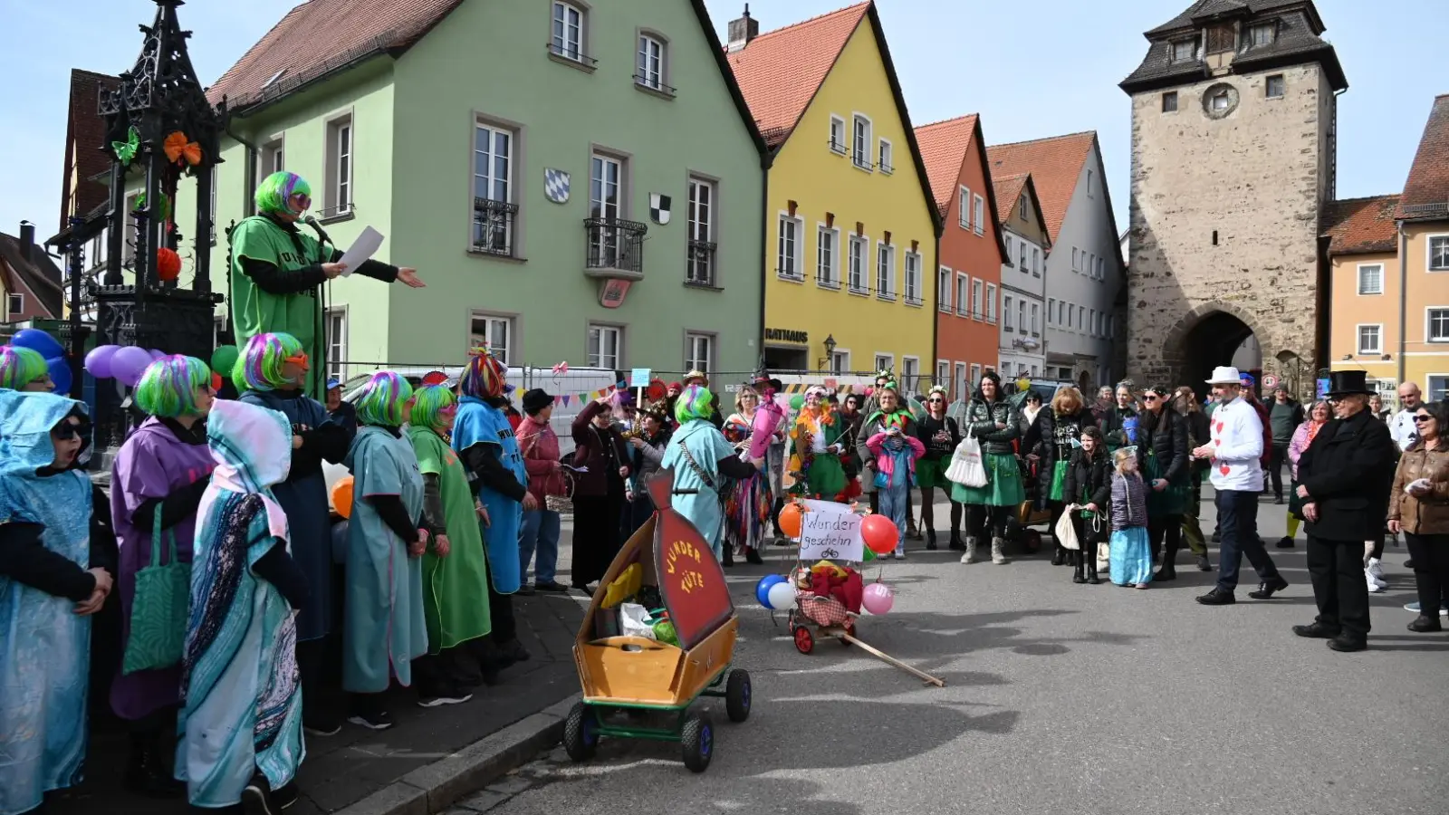 Büttenrede vom Röhrenbrunnen aus: Christina Gurdan-Berndt, flankiert von ihren bunten „Wundertüten“, las vor allem Bürgermeister Markus Liebich (rechts, mit weißem Hut) die Leviten. (Foto: Wolfgang Grebenhof)