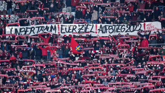 Fans des 1. FC Kaiserslautern halten ein Transparent mit der Aufschrift „Unser Traum! Euer Ziel! Aufstieg 2022!“ in die Höhe. (Foto: Uwe Anspach/dpa)