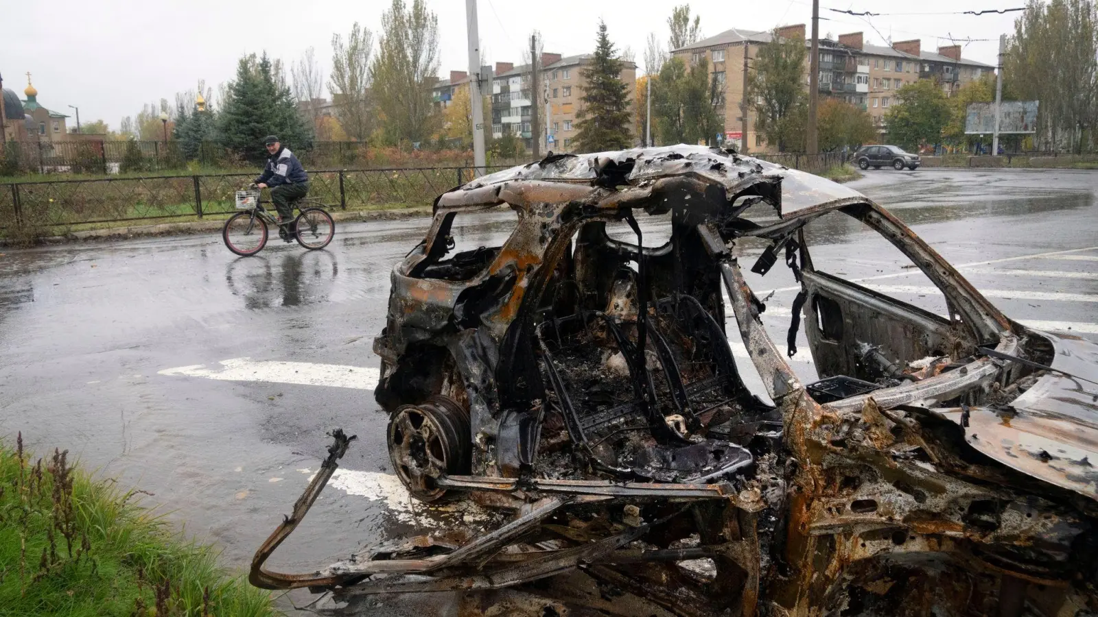 Ein Mann fährt in Bachmut mit seinem Fahrrad an einem Auto vorbei, das durch Beschuss zerstört wurde. (Foto: Efrem Lukatsky/AP/dpa)