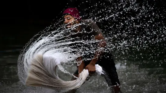 Ein Mann wäscht Textilien am Ufer des Brahmaputra-Flusses in Indien. (Foto: Anupam Nath/AP/dpa)