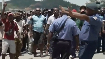 Das Videostandbild zeigt zwei Polizisten neben einer aufgebrachten Menschenmenge in Port Moresby. (Foto: Uncredited/Australian Broadcasting Corp/AP/dpa)