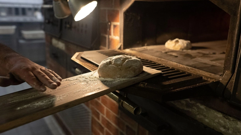 Das Einbringen eines geformten Teiglings in den heißen Backofen mit Hilfe eines Brotschiebers wird „Einschießen“ genannt. Oft wird der Vorgang von einem kurzen Ruck begleitet, damit das Brot auf dem Backstein oder Backblech landet.  (Foto: Swen Pförtner/dpa/dpa-tmn)