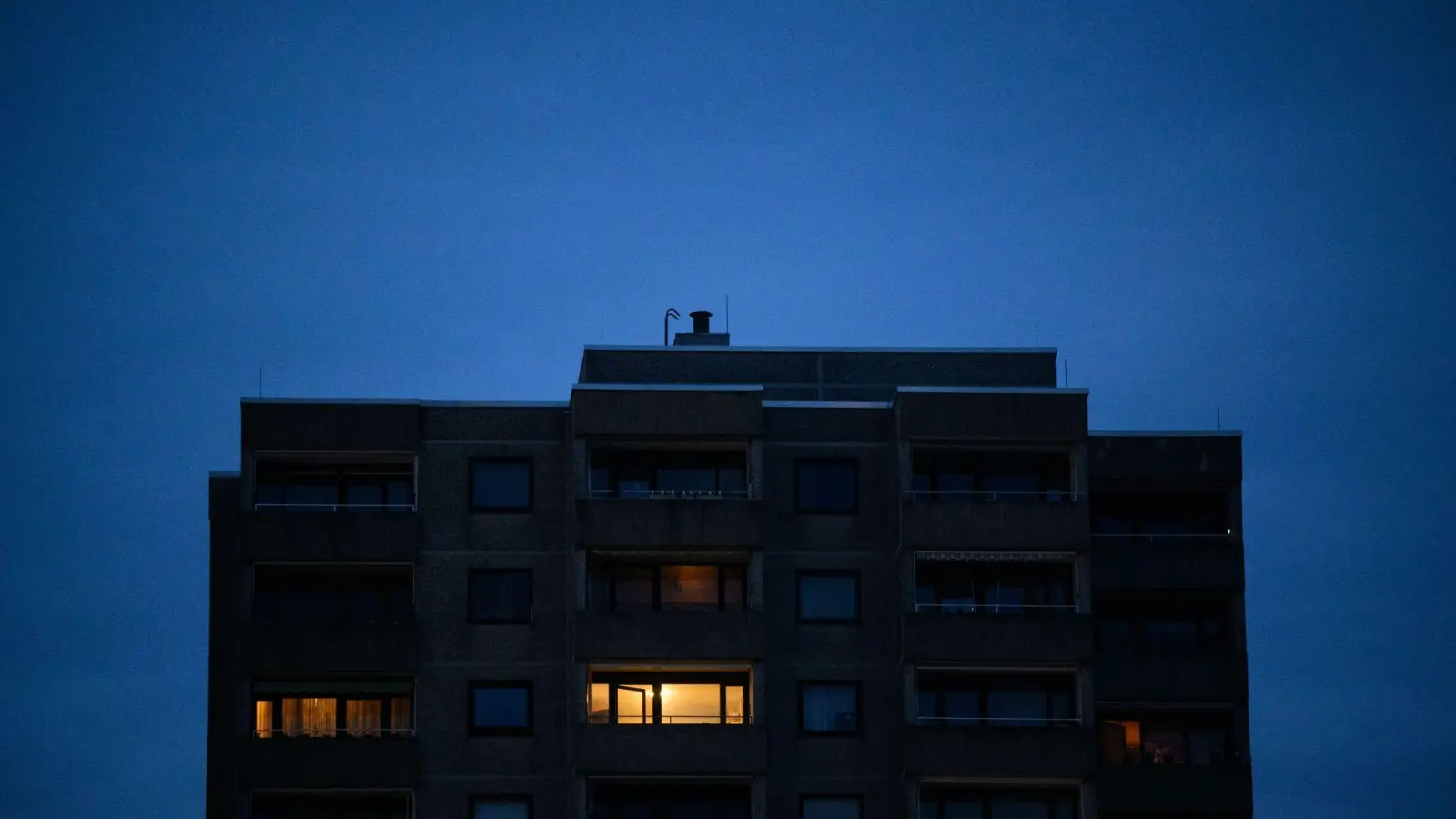 Licht brennt nur in einzelnen Wohnungen eines Mehrfamilienhauses. (Foto: Julian Stratenschulte/dpa/Symbolbild)