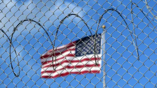 Eine US-Flagge hinter Zaun und Stacheldraht auf dem Marinestützpunkt Guantánamo Bay auf Kuba. Hier betreiben die USA seit mehr als 21 Jahren ein umstrittenes Gefangenenlager. (Foto: Magdalena Miriam Tröndle/dpa)