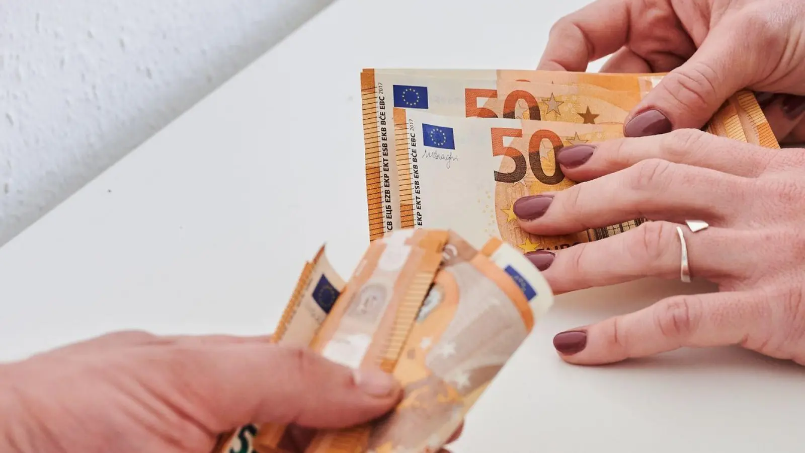 Eine Männerhand hält ein Bündel 50-Euro-Scheine, während eine Frauenhand nur wenige 50-Euro-Scheine hält. (Foto: Annette Riedl/dpa)