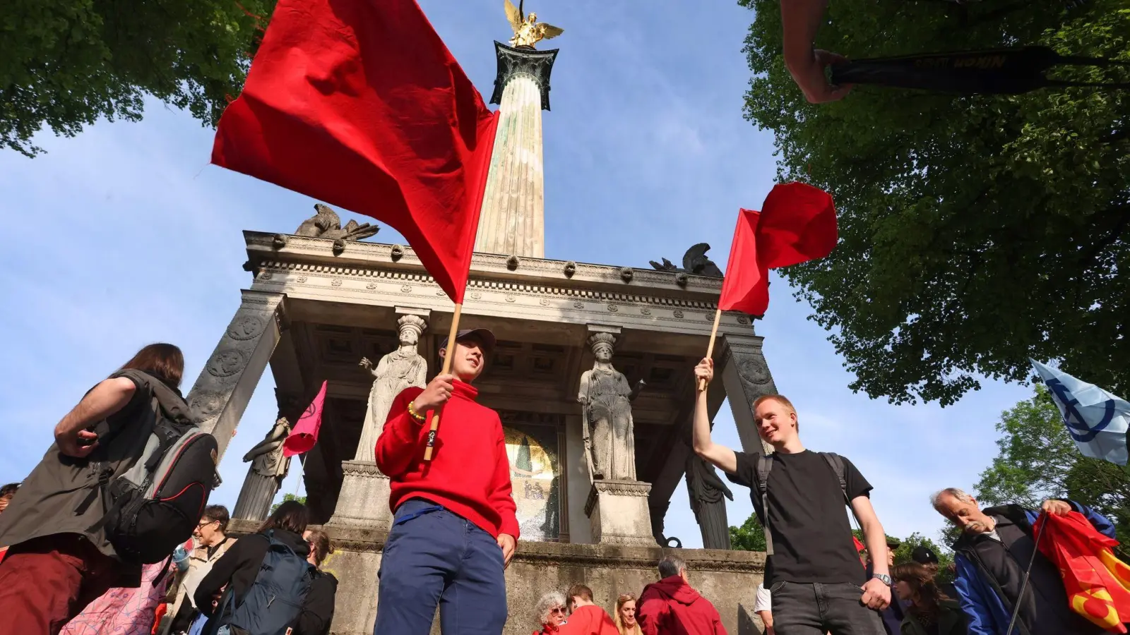 Teilnehmer einer Solidaritätskundgebung für die Letzte Generation schwenken am Friedensengel rote Fahnen. (Foto: Karl-Josef Hildenbrand/dpa)