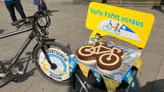 Ein Rad und ein Kuchen in Form eines Fahrrads stehen vor dem Justizpalast. (Foto: Jacqueline Melcher/dpa)
