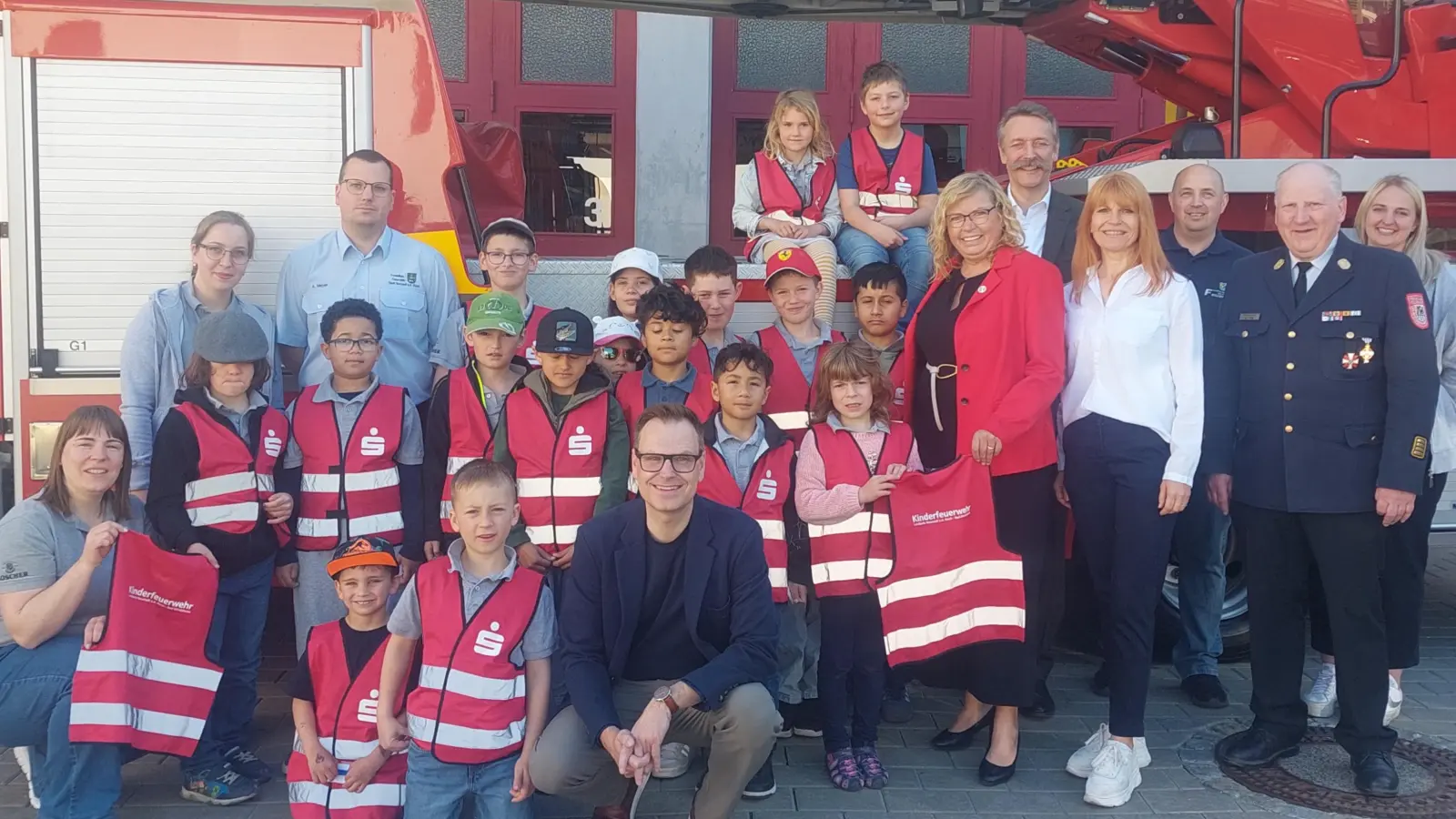 Mit Feuereifer bei der Feuerwehr: Die Neustädter Nachwuchskräfte stellten sich in ihren neuen knallroten Warnwesten zusammen mit ihren prominenten Gästen für ein gemeinsames Foto auf – den passenden Hintergrund inklusive.  (Foto: Sandra Buchwald)