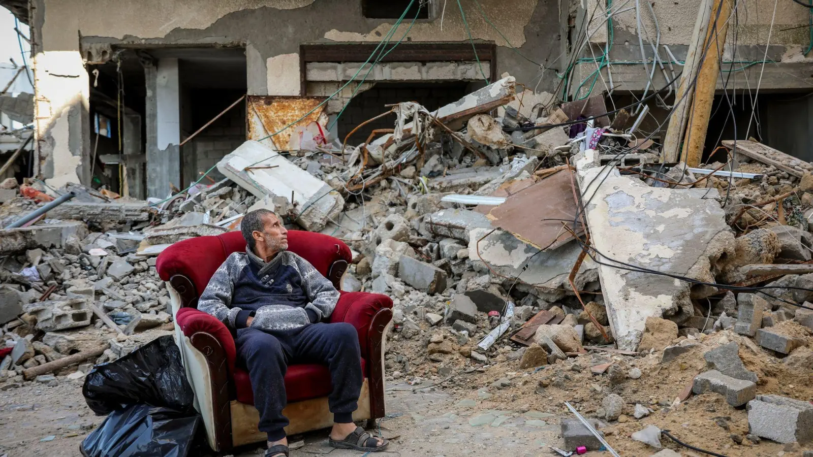 Ein palästinensischer Mann sitzt in einem Sessel vor einem zerstörten Gebäude in Gaza-Stadt. (Foto: Mohammed Hajjar/AP/dpa)