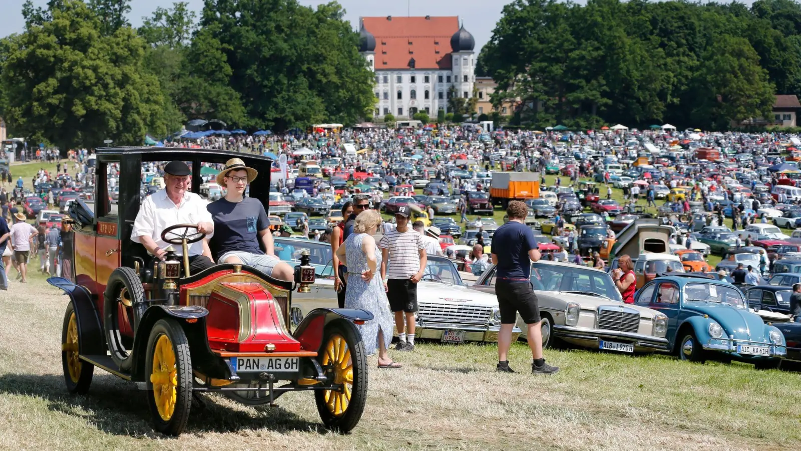 Teilnehmer von Südbayerns größtem Oldtimer-Treffen stehen mit ihren Fahrzeugen vor Schloss Maxlrain. (Foto: Uwe Lein/dpa)