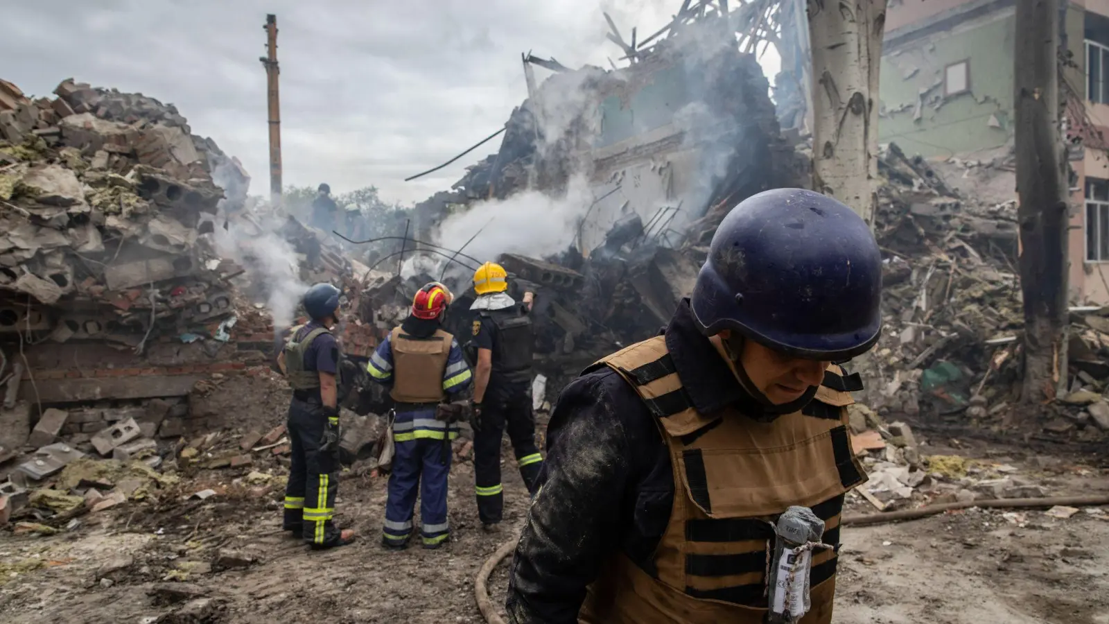 Ukrainische Feuerwehrleute stehen vor einer zerstörten Schule nach einem Beschuss. (Foto: Alex Chan Tsz Yuk/SOPA Images via ZUMA Press Wire/dpa)