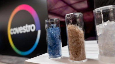 Eine deutsche Firma wird arabisch: Das Logo des Spezialchemie-Konzerns in einem Firmen-Showroom, davor Gläser mit Covestro-Materialien.  (Foto: Fabian Strauch/dpa)