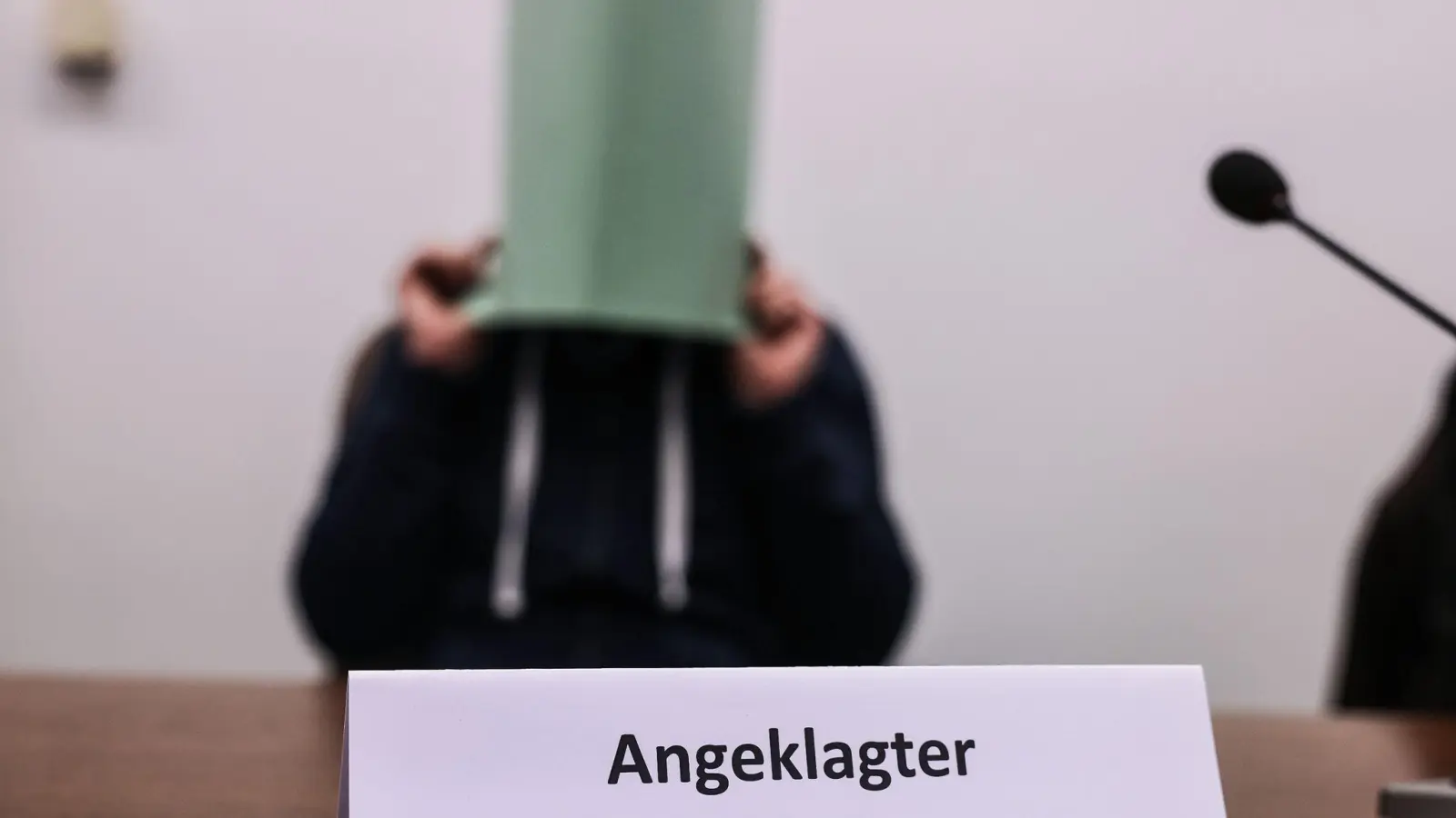 Der Angeklagte im Missbrauchskomplex Wermelskirchen hält sich im Gerichtssaal eine Mappe vor das Gesicht. (Foto: Oliver Berg/dpa)