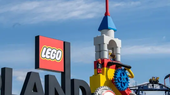 Neben dem Logo am Eingang zum Legoland ist eine Achterbahn (r) zu sehen. Bei einem Unfall auf einer Achterbahn im Legoland sind im August 2022 im schwäbischen Günzburg 31 Menschen verletzt worden. (Foto: Stefan Puchner/dpa)