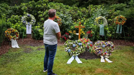 Ein Mann steht in stillem Gedenken an dem mit Kränzen und Blumen geschmückten schlichten Grab der Fußballlegende Uwe Seeler. (Foto: Christian Charisius/dpa)