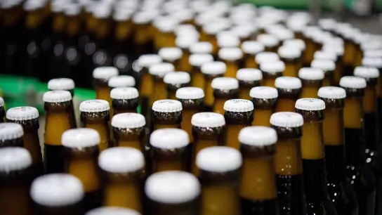 Bierflaschen mit Kronkorken laufen durch die Produktion einer Brauerei. Die weltweite Bierproduktion könnte im laufenden Jahr zurückgehen. (Foto: Rainer Jensen/dpa)